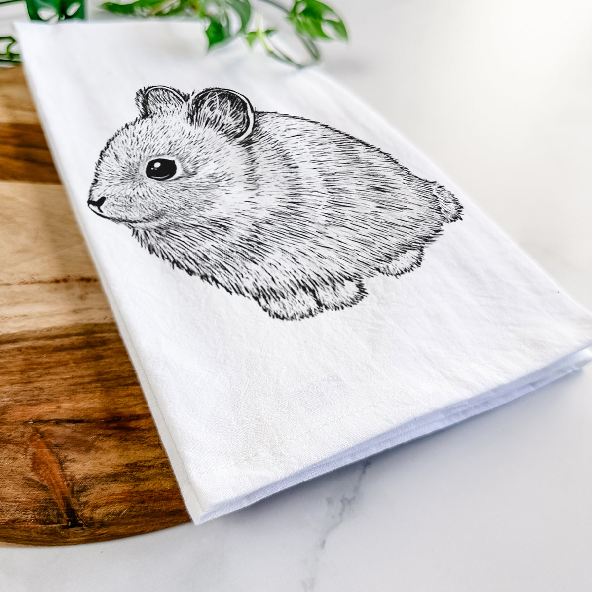 Close-up of a folded white tea towel on a wooden board, showing a detailed black ink illustration of a round, fluffy pygmy rabbit.
