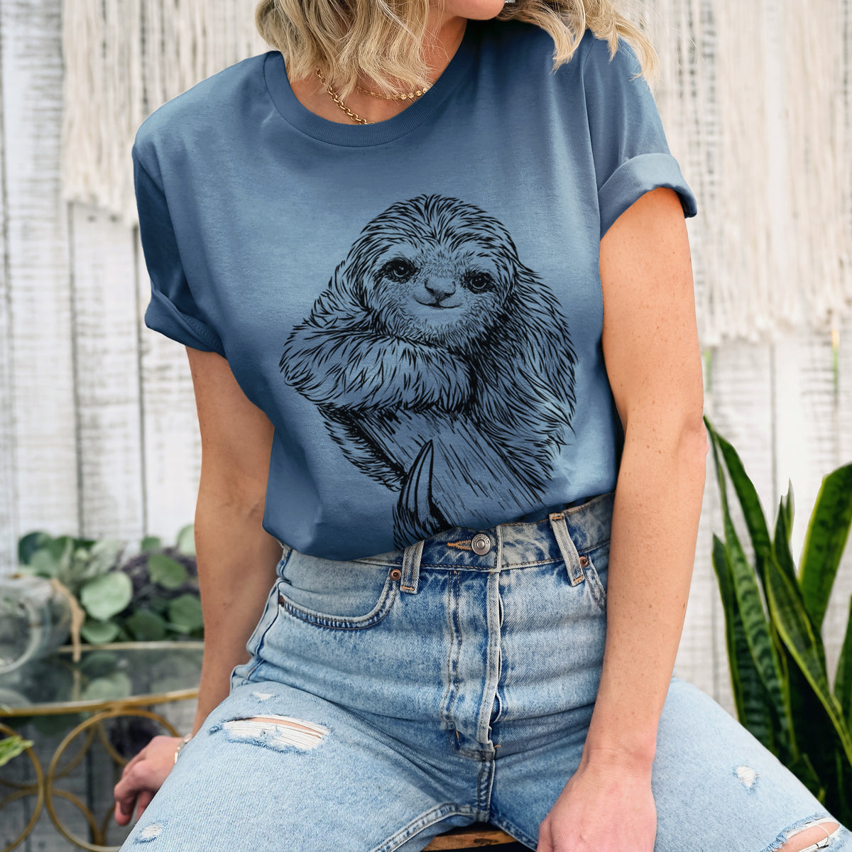 Woman wearing a steel blue lightweight cotton t-shirt printed with a detailed black ink illustration of a smiling pygmy three-toed sloth hanging from a branch.