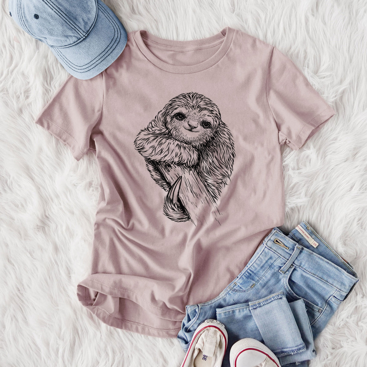 Women's relaxed fit cotton t-shirt printed with a detailed black ink illustration of a smiling pygmy three-toed sloth hanging from a branch, styled flat on a white faux fur rug with jeans.
