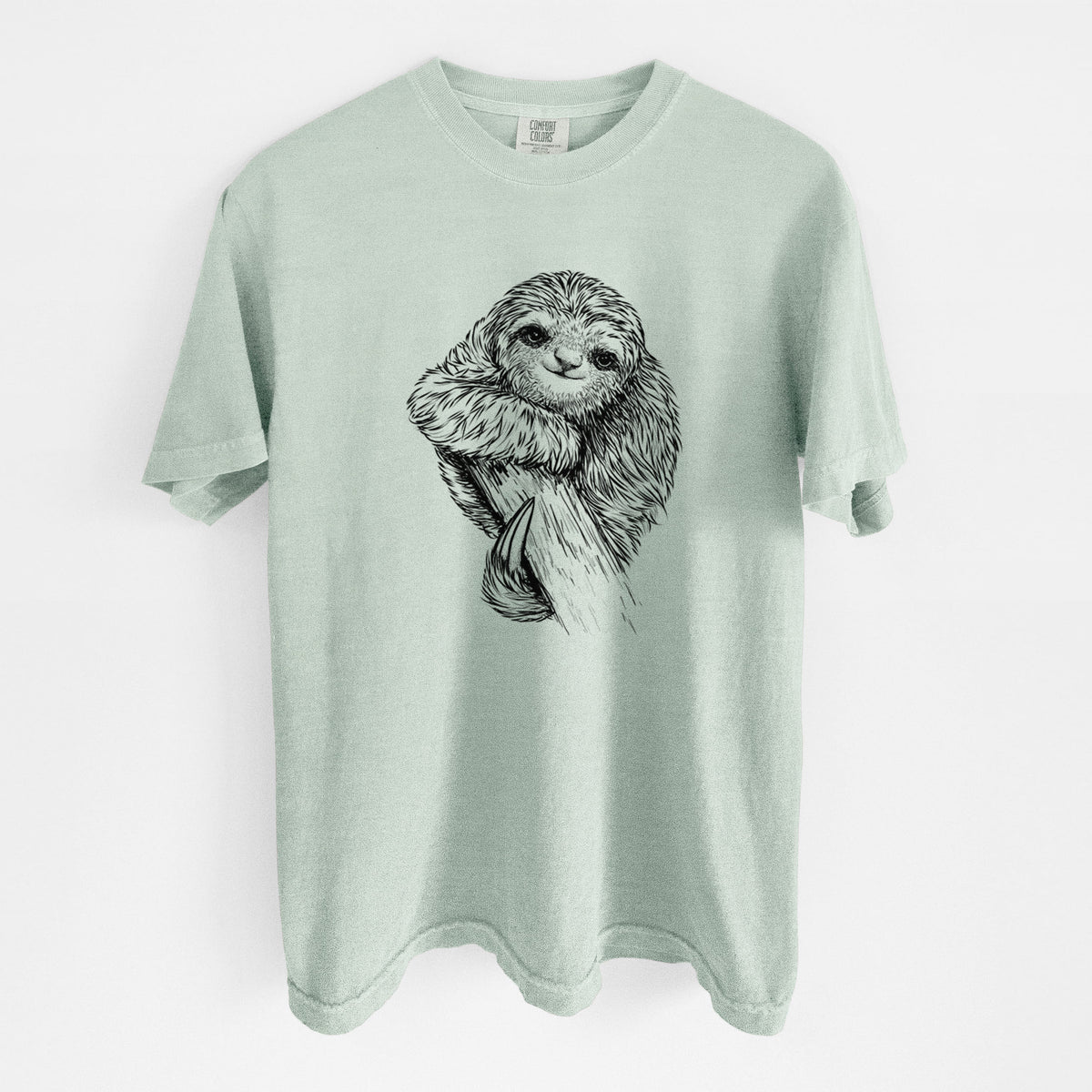 Bay green Comfort Colors t-shirt laid flat, printed with a detailed black ink illustration of a smiling pygmy three-toed sloth hanging from a branch.