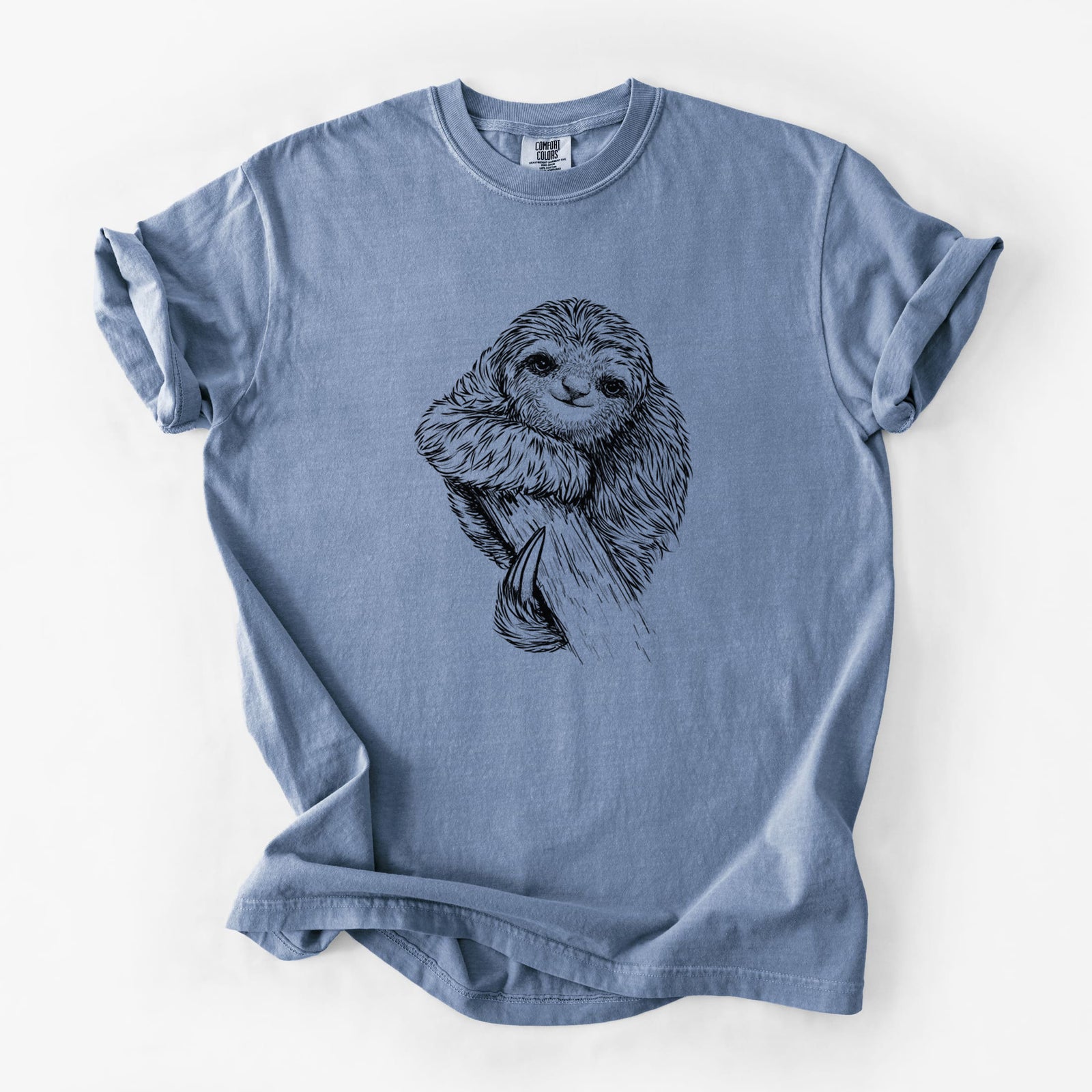 Blue jean Comfort Colors t-shirt laid flat, printed with a detailed black ink illustration of a smiling pygmy three-toed sloth hanging from a branch.
