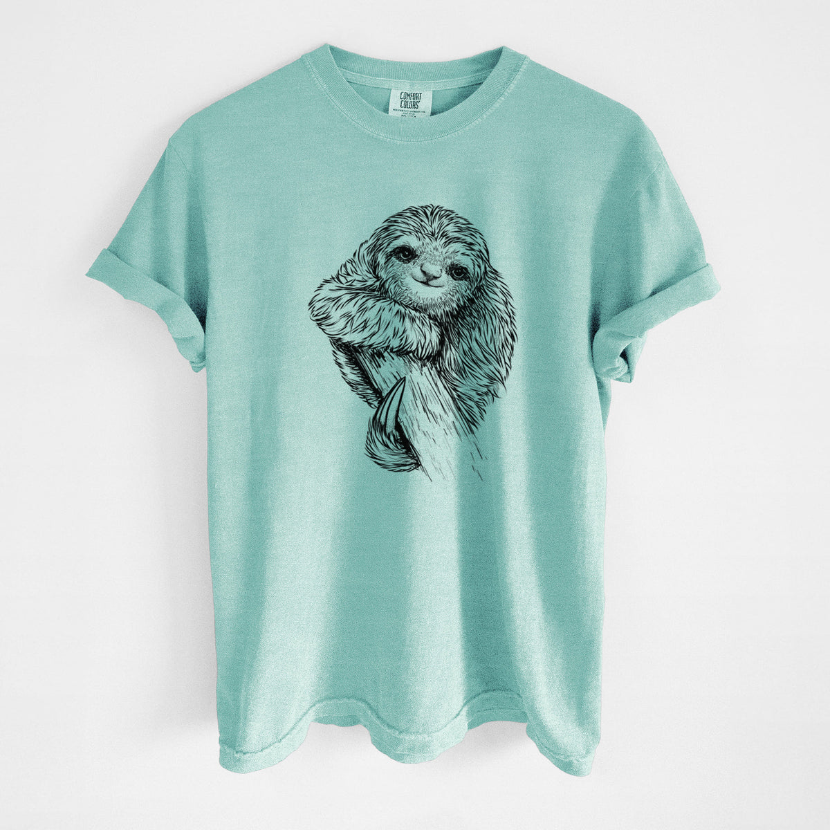 Chalky mint Comfort Colors t-shirt laid flat, printed with a detailed black ink illustration of a smiling pygmy three-toed sloth hanging from a branch.