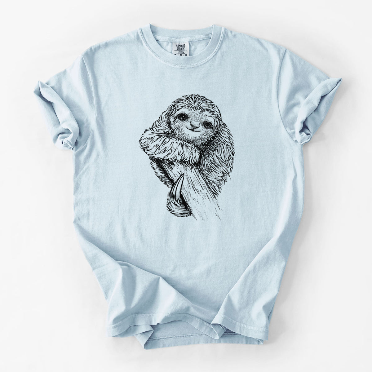 Chambray blue Comfort Colors t-shirt laid flat, printed with a detailed black ink illustration of a smiling pygmy three-toed sloth hanging from a branch.