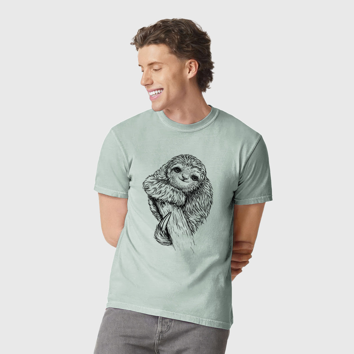 Man wearing a Comfort Colors t-shirt printed with a detailed black ink illustration of a smiling pygmy three-toed sloth hanging from a branch.