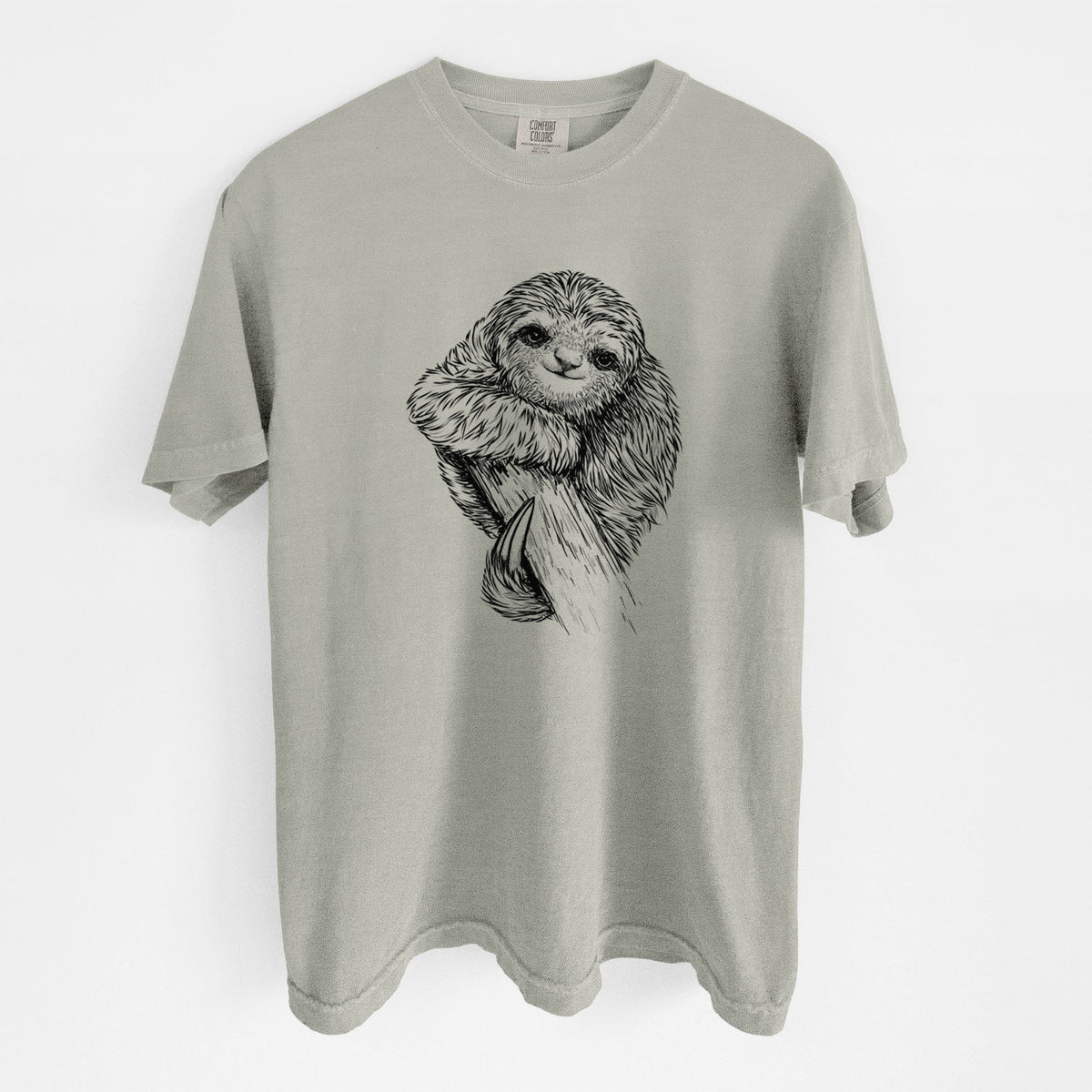 Sandstone beige Comfort Colors t-shirt laid flat, printed with a detailed black ink illustration of a smiling pygmy three-toed sloth hanging from a branch.