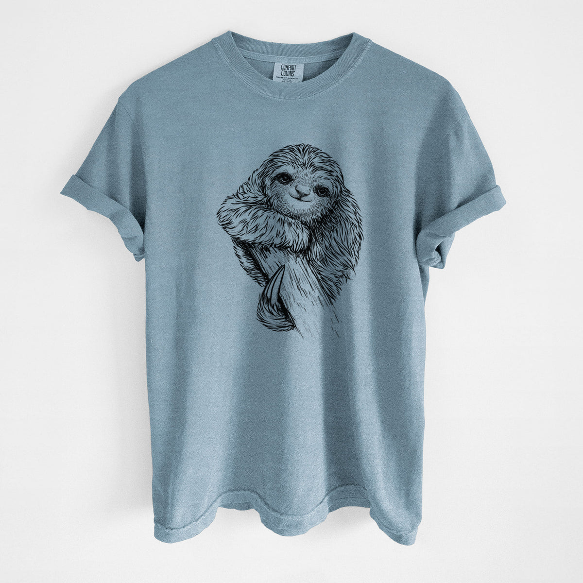 Steel blue Comfort Colors t-shirt laid flat, printed with a detailed black ink illustration of a smiling pygmy three-toed sloth hanging from a branch.