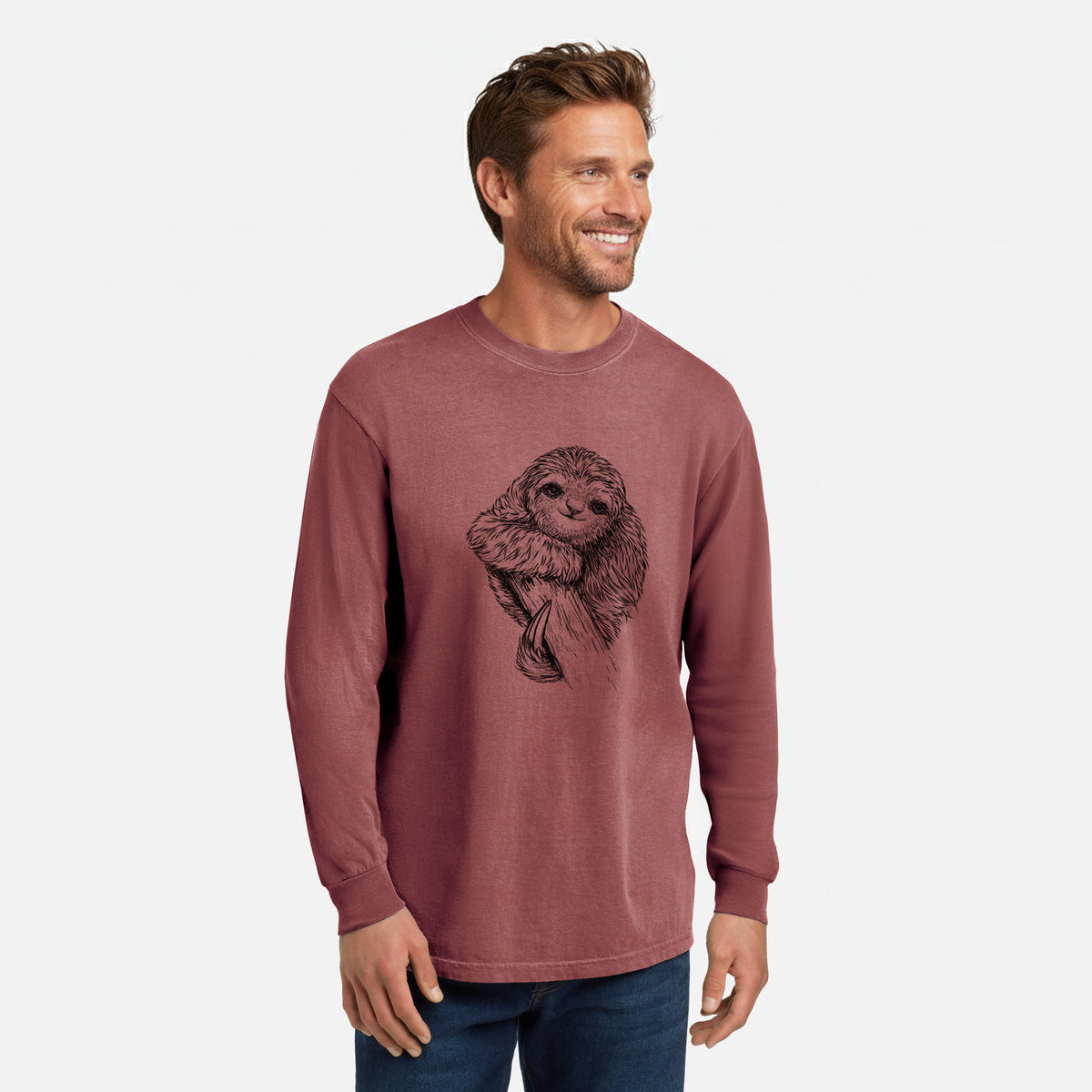 Brick red Comfort Colors long sleeve shirt printed with a detailed black ink illustration of a smiling pygmy three-toed sloth hanging from a branch, shown in a lifestyle photo.