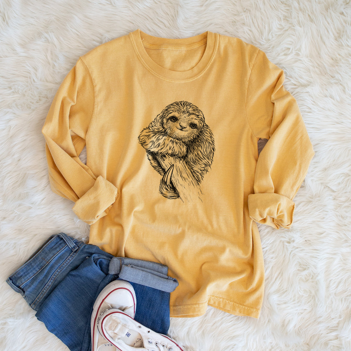 Golden wheat yellow Comfort Colors long sleeve shirt printed with a detailed black ink illustration of a smiling pygmy three-toed sloth hanging from a branch, shown in a lifestyle photo.