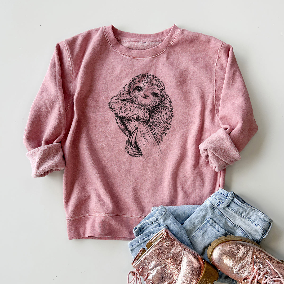 Youth crewneck sweatshirt printed with a detailed black ink illustration of a smiling pygmy three-toed sloth hanging from a branch, styled flat with jeans and boots.