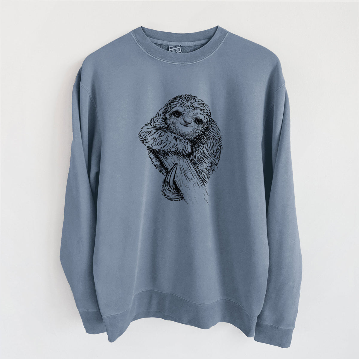 Slate blue pigment dyed crewneck sweatshirt laid flat, printed with a detailed black ink illustration of a smiling pygmy three-toed sloth hanging from a branch.