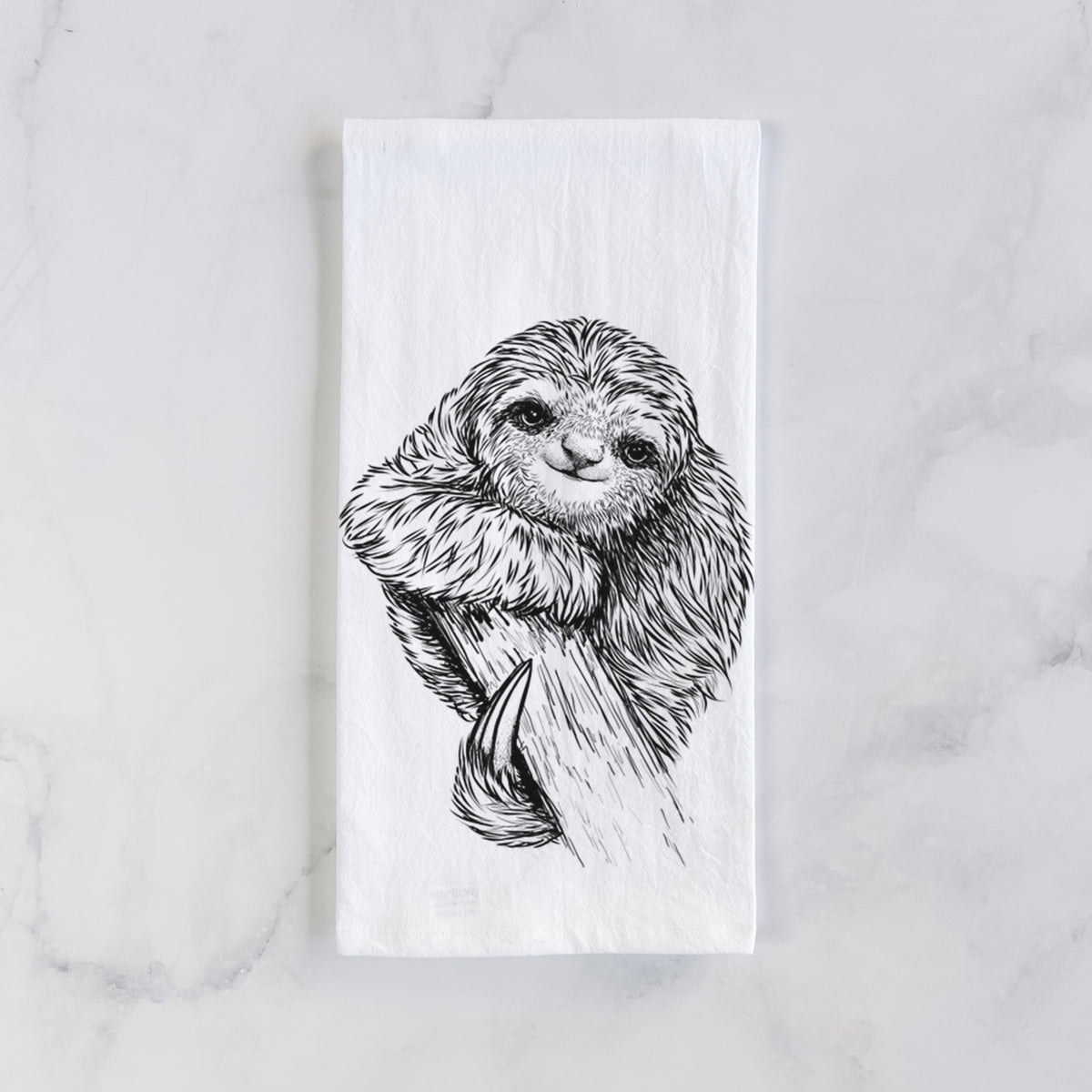 White cotton tea towel laid flat on marble, printed with a detailed black ink illustration of a smiling pygmy three-toed sloth hanging from a branch.