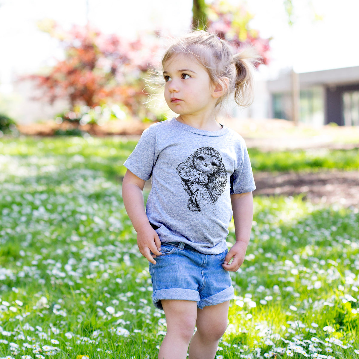 Toddler girl walking outdoors wearing a t-shirt printed with a detailed black ink illustration of a smiling pygmy three-toed sloth hanging from a branch.