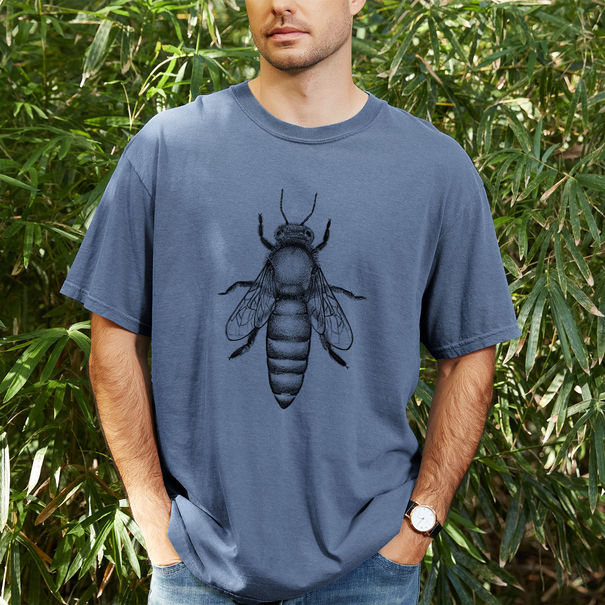 Man wearing a Comfort Colors t-shirt printed with a detailed black ink illustration of a queen honey bee, seen from above, outdoors.