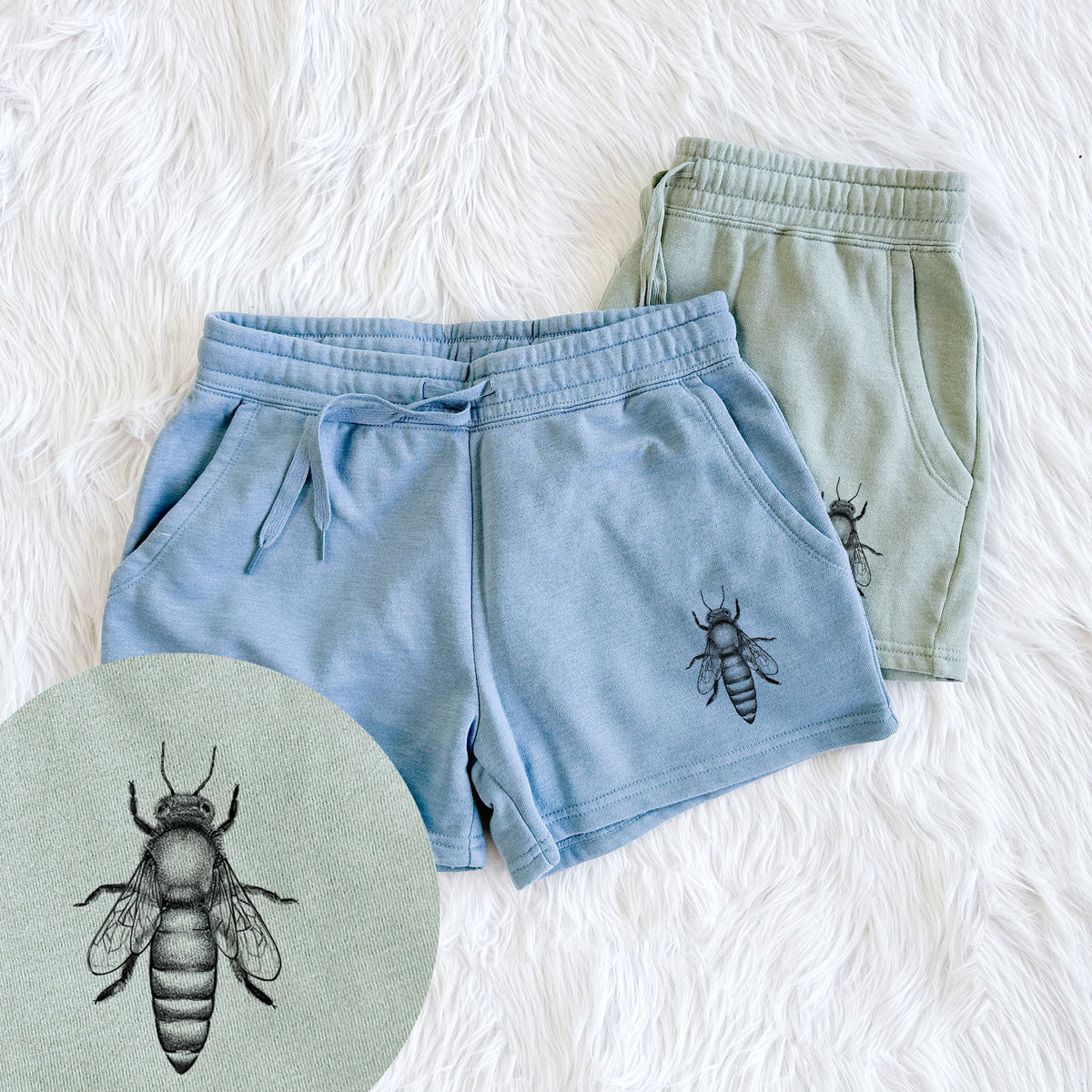 Two pairs of Cali Wave shorts in different colors printed with a detailed black ink illustration of a queen honey bee, seen from above, with a close-up of the print.