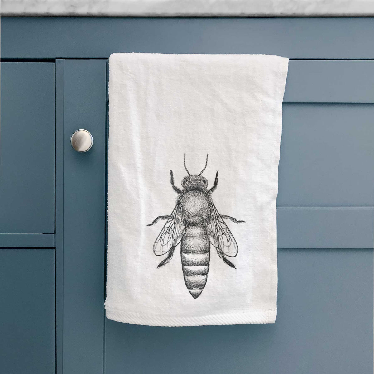 White hand towel printed with a detailed black ink illustration of a queen honey bee, seen from above, hanging on a cabinet door.