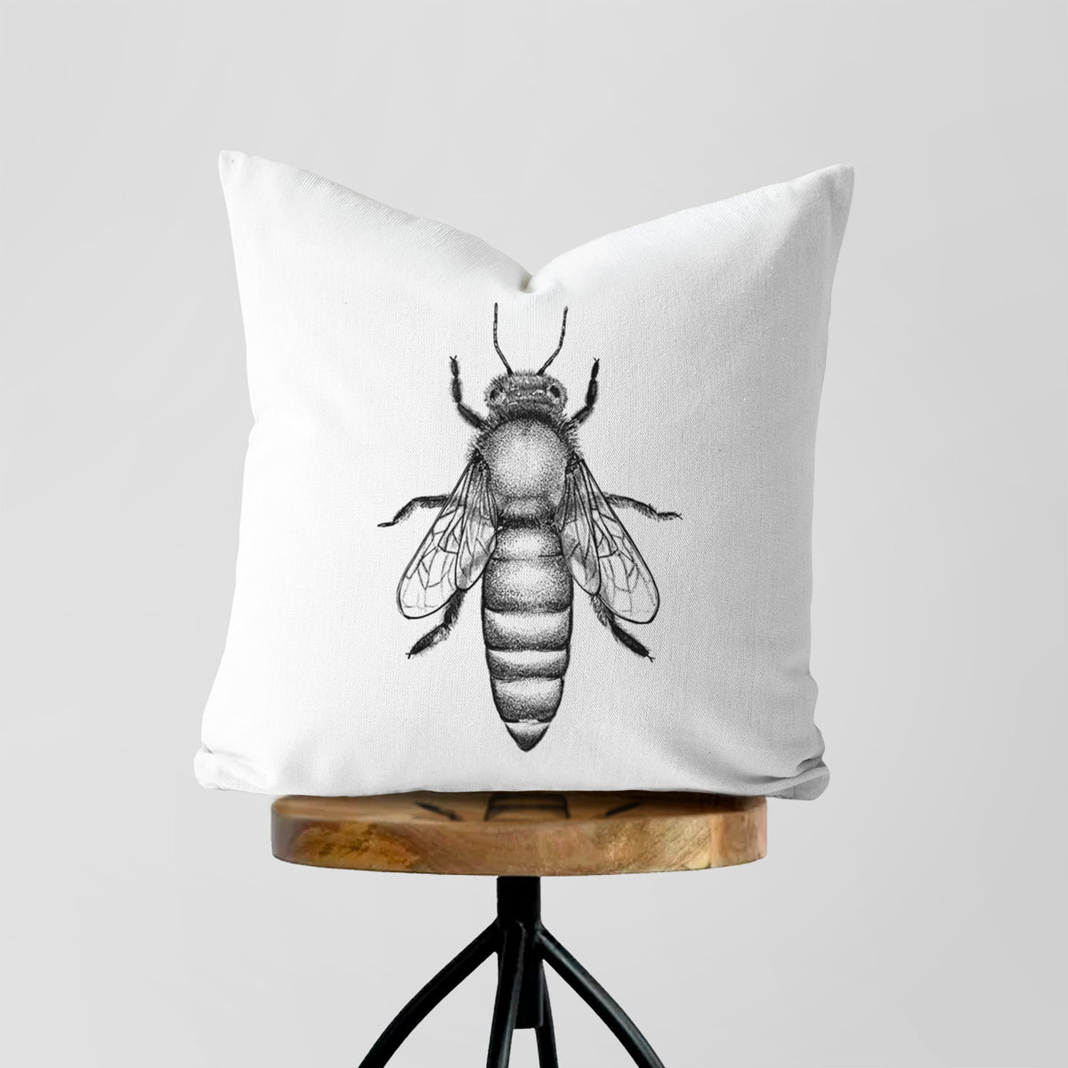 White pillow cover printed with a detailed black ink illustration of a queen honey bee, seen from above, on a wooden stool.