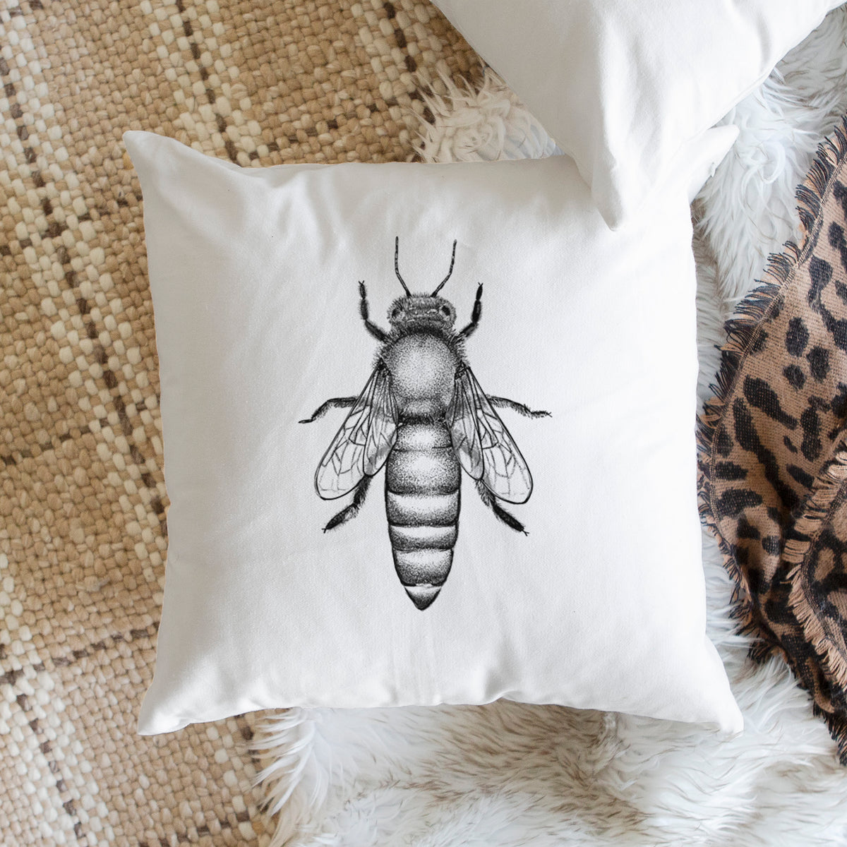 White pillow cover printed with a detailed black ink illustration of a queen honey bee, seen from above, on a woven chair.