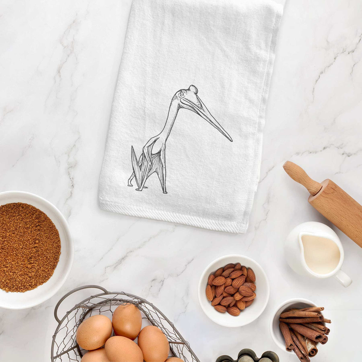 White hand towel printed with a black ink illustration of a Quetzalcoatlus pterosaur standing on all fours, hanging on a cabinet door.
