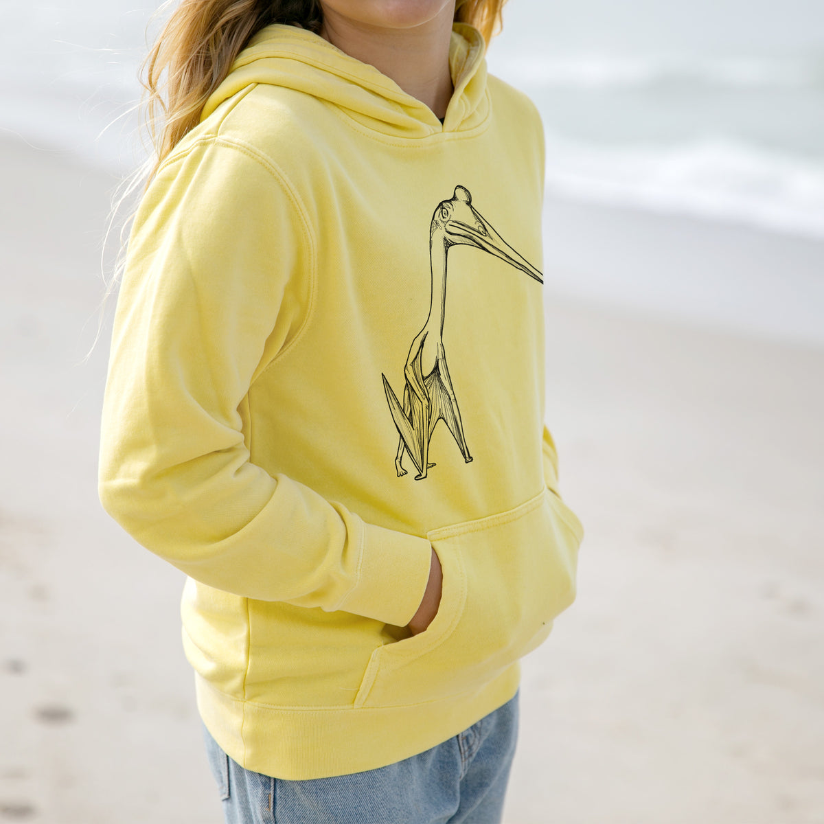 Girl wearing a youth pigment dyed hoodie printed with a black ink illustration of a Quetzalcoatlus pterosaur standing on all fours.