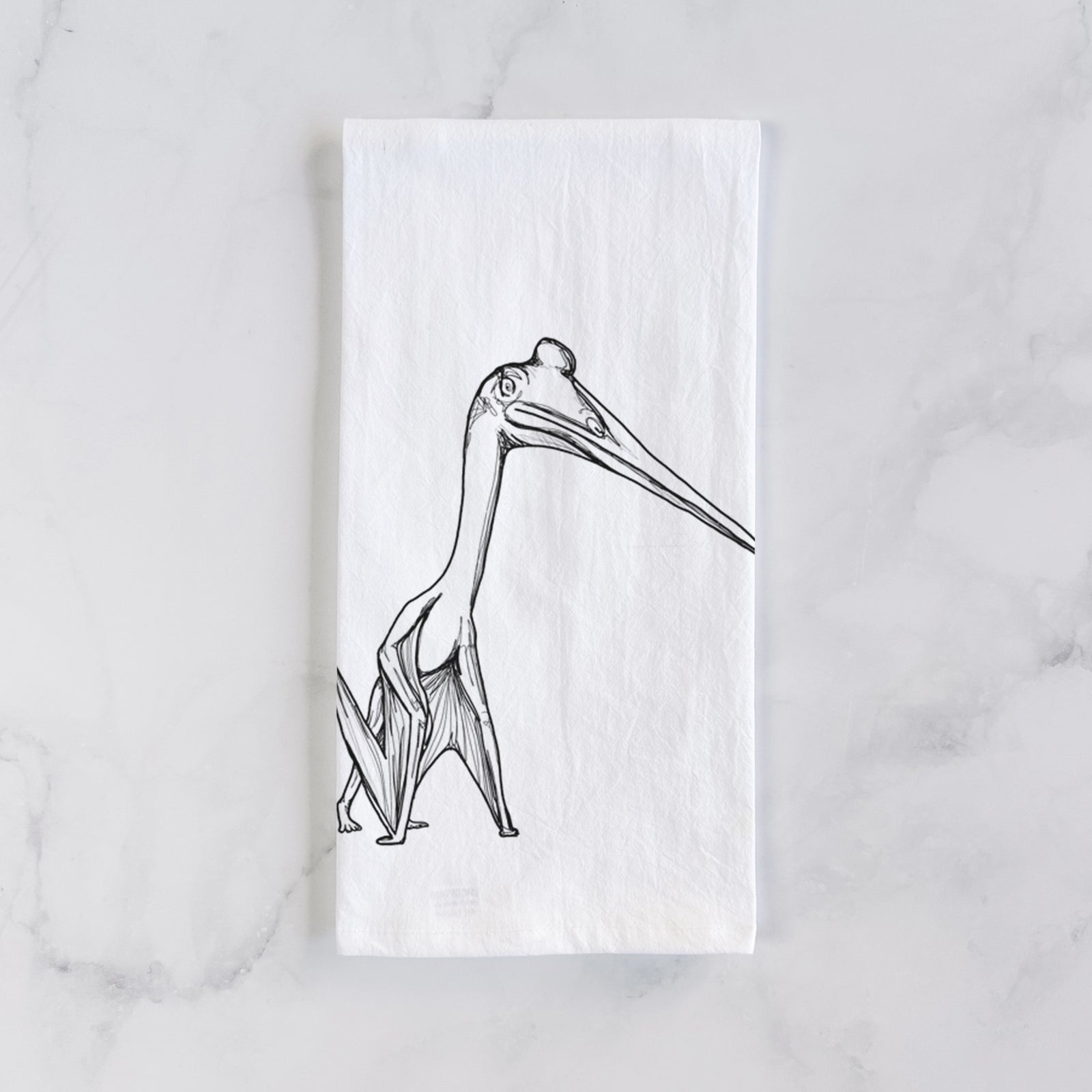 White cotton tea towel printed with a black ink illustration of a Quetzalcoatlus pterosaur standing on all fours, on a marble counter beside a round wooden cutting board and greenery.