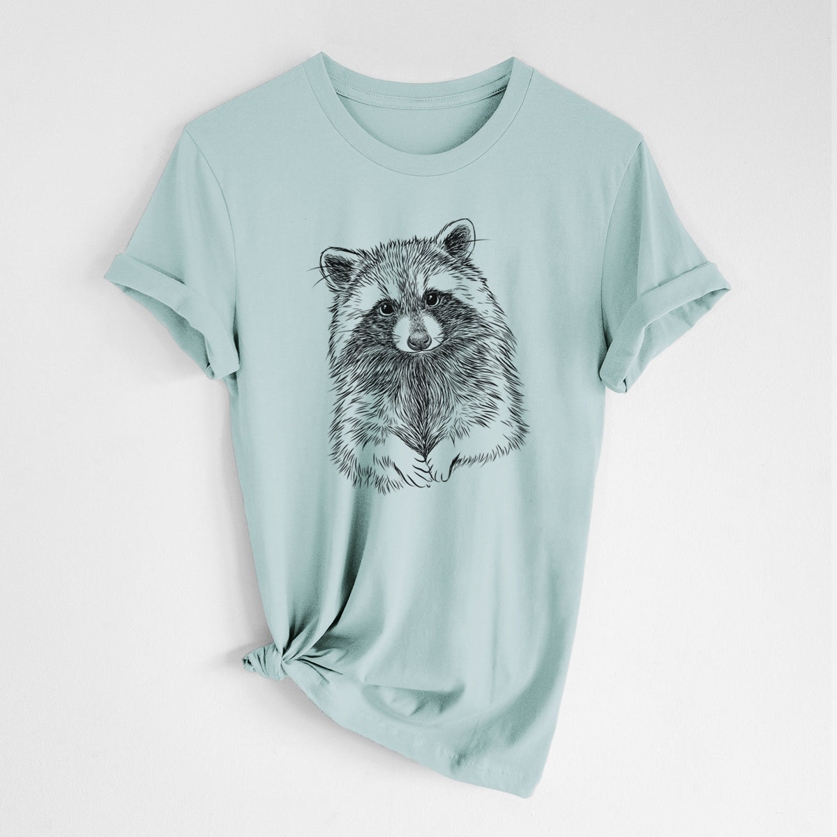 Dusty blue lightweight cotton t-shirt laid flat with the sleeves rolled, printed with a detailed black ink portrait of a raccoon with its front paws resting in front of it.