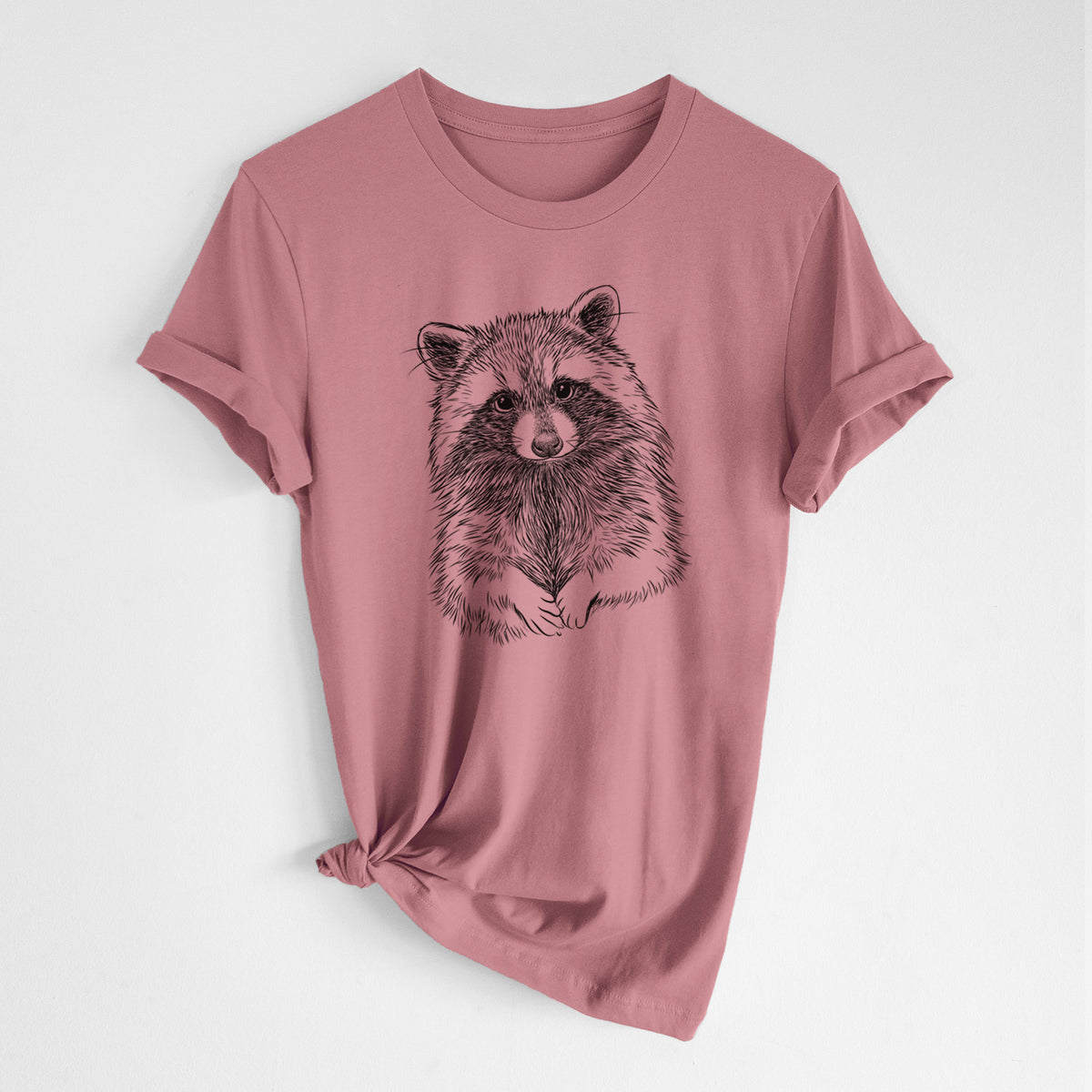 Mauve pink lightweight cotton t-shirt laid flat with the sleeves rolled, printed with a detailed black ink portrait of a raccoon with its front paws resting in front of it.