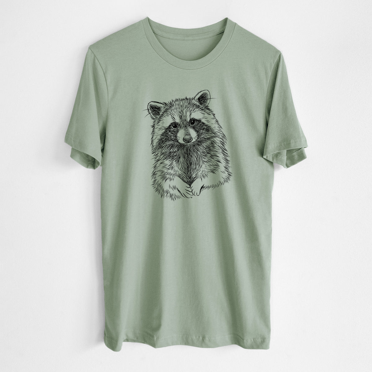 Sage green lightweight cotton t-shirt laid flat, printed with a detailed black ink portrait of a raccoon with its front paws resting in front of it.