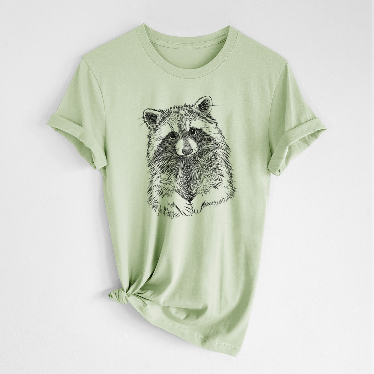 Spring green lightweight cotton t-shirt laid flat with the sleeves rolled, printed with a detailed black ink portrait of a raccoon with its front paws resting in front of it.