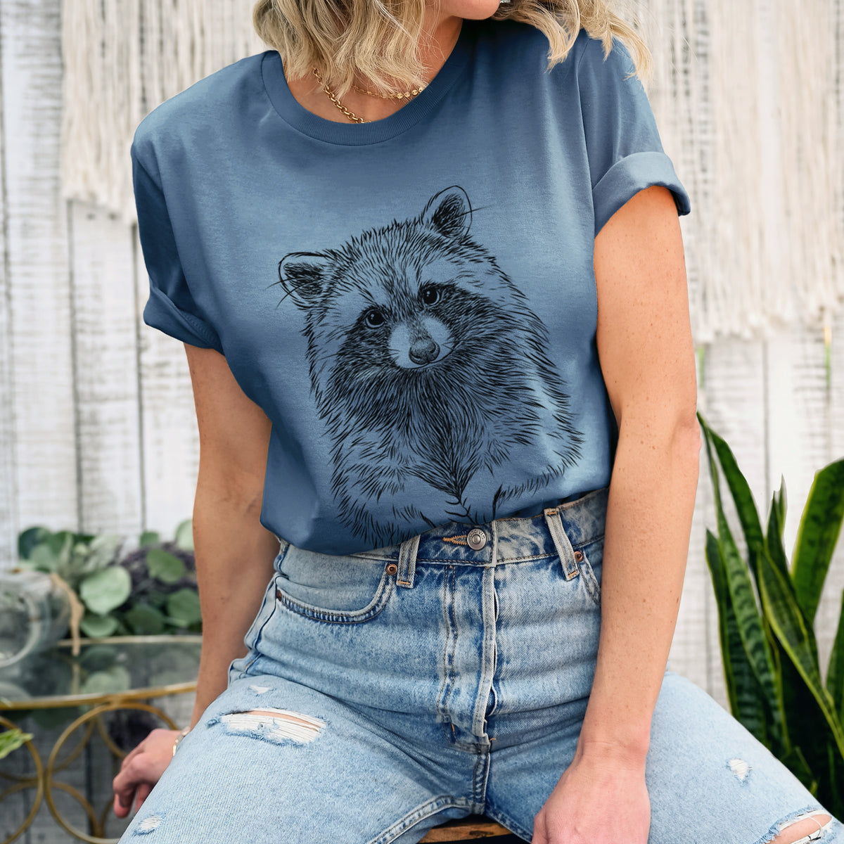 Woman wearing a steel blue lightweight cotton t-shirt printed with a detailed black ink portrait of a raccoon with its front paws resting in front of it.