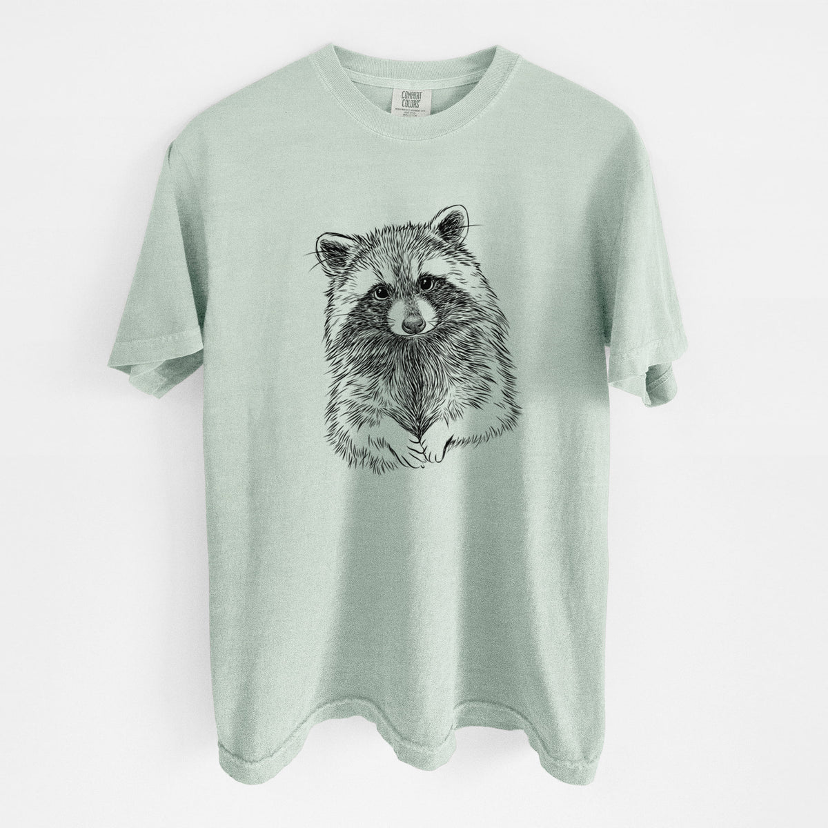 Bay green Comfort Colors t-shirt laid flat, printed with a detailed black ink portrait of a raccoon with its front paws resting in front of it.