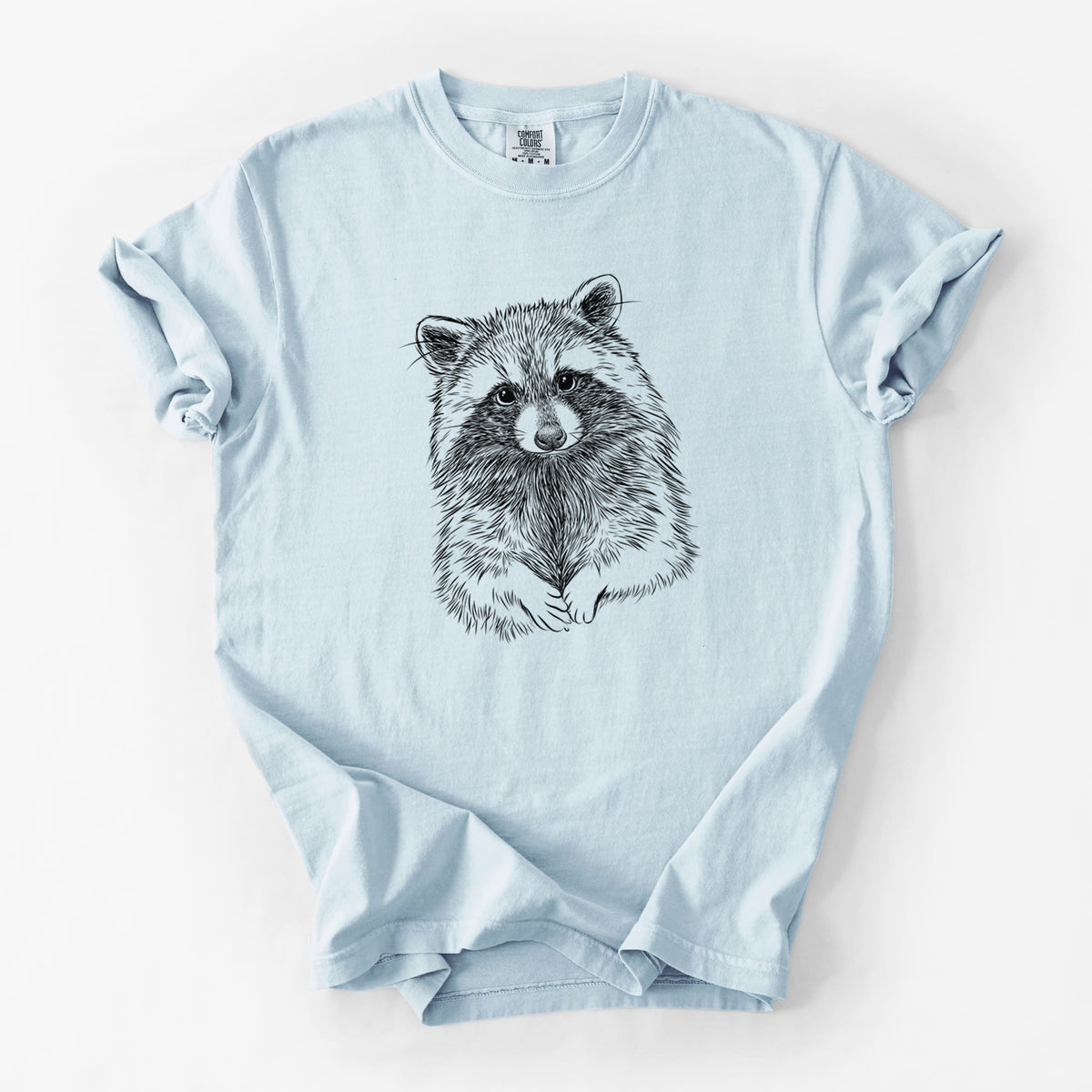 Chambray blue Comfort Colors t-shirt laid flat, printed with a detailed black ink portrait of a raccoon with its front paws resting in front of it.