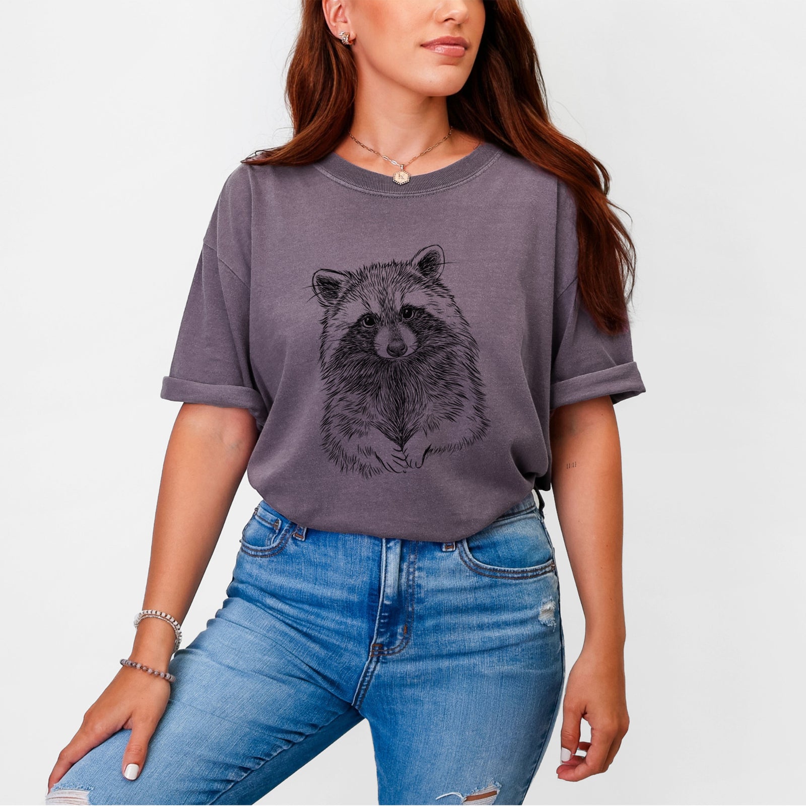 Blue jean Comfort Colors t-shirt laid flat, printed with a detailed black ink portrait of a raccoon with its front paws resting in front of it.