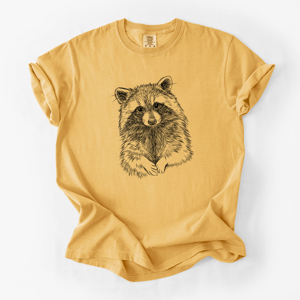 Golden wheat yellow Comfort Colors t-shirt laid flat, printed with a detailed black ink portrait of a raccoon with its front paws resting in front of it.