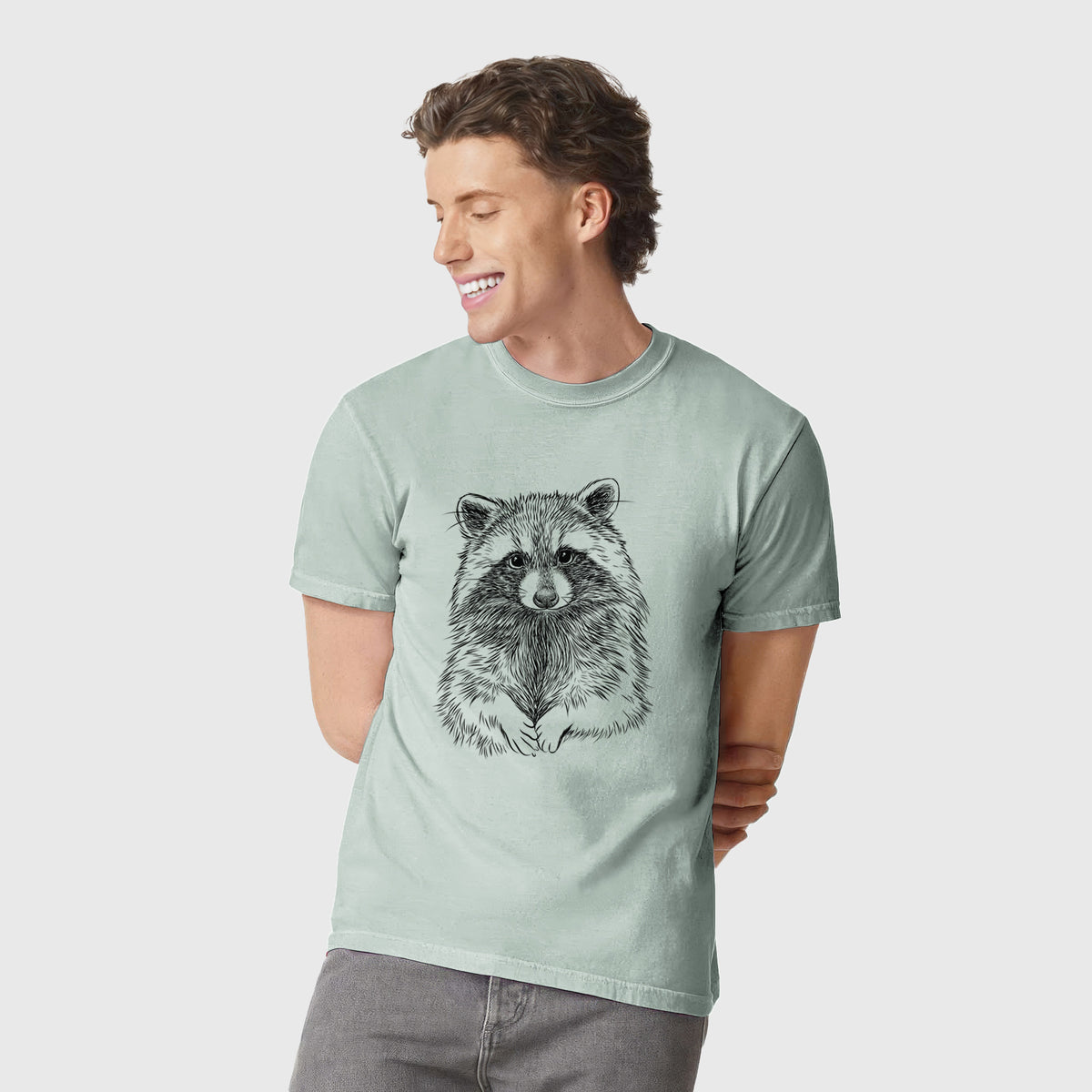 Man wearing a Comfort Colors t-shirt printed with a detailed black ink portrait of a raccoon with its front paws resting in front of it.