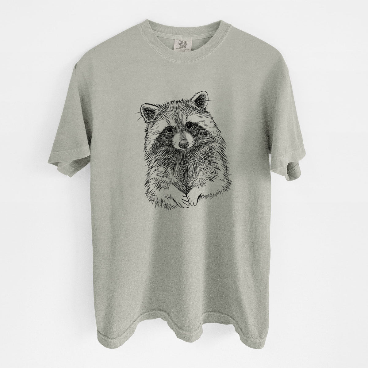 Sandstone beige Comfort Colors t-shirt laid flat, printed with a detailed black ink portrait of a raccoon with its front paws resting in front of it.
