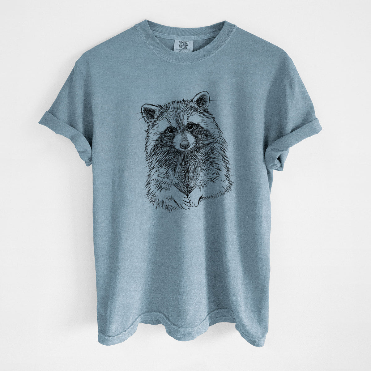 Steel blue Comfort Colors t-shirt laid flat, printed with a detailed black ink portrait of a raccoon with its front paws resting in front of it.