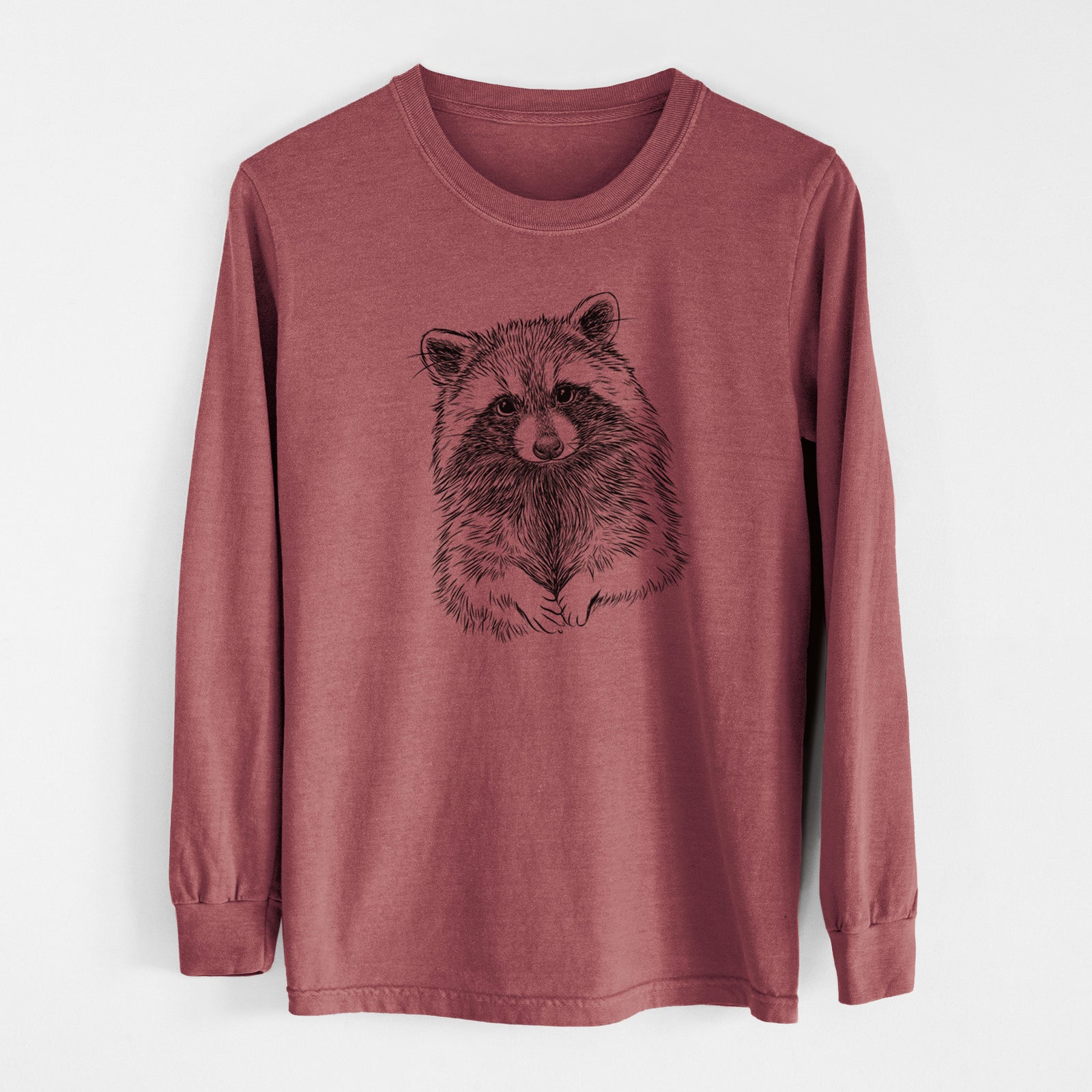 Brick red Comfort Colors long sleeve shirt laid flat, printed with a detailed black ink portrait of a raccoon with its front paws resting in front of it.