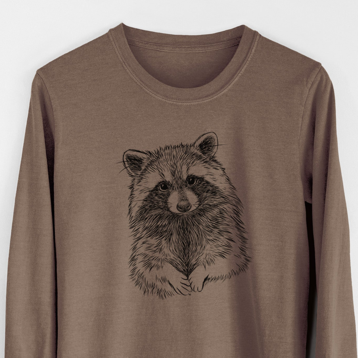 Espresso brown Comfort Colors long sleeve shirt laid flat, printed with a detailed black ink portrait of a raccoon with its front paws resting in front of it.