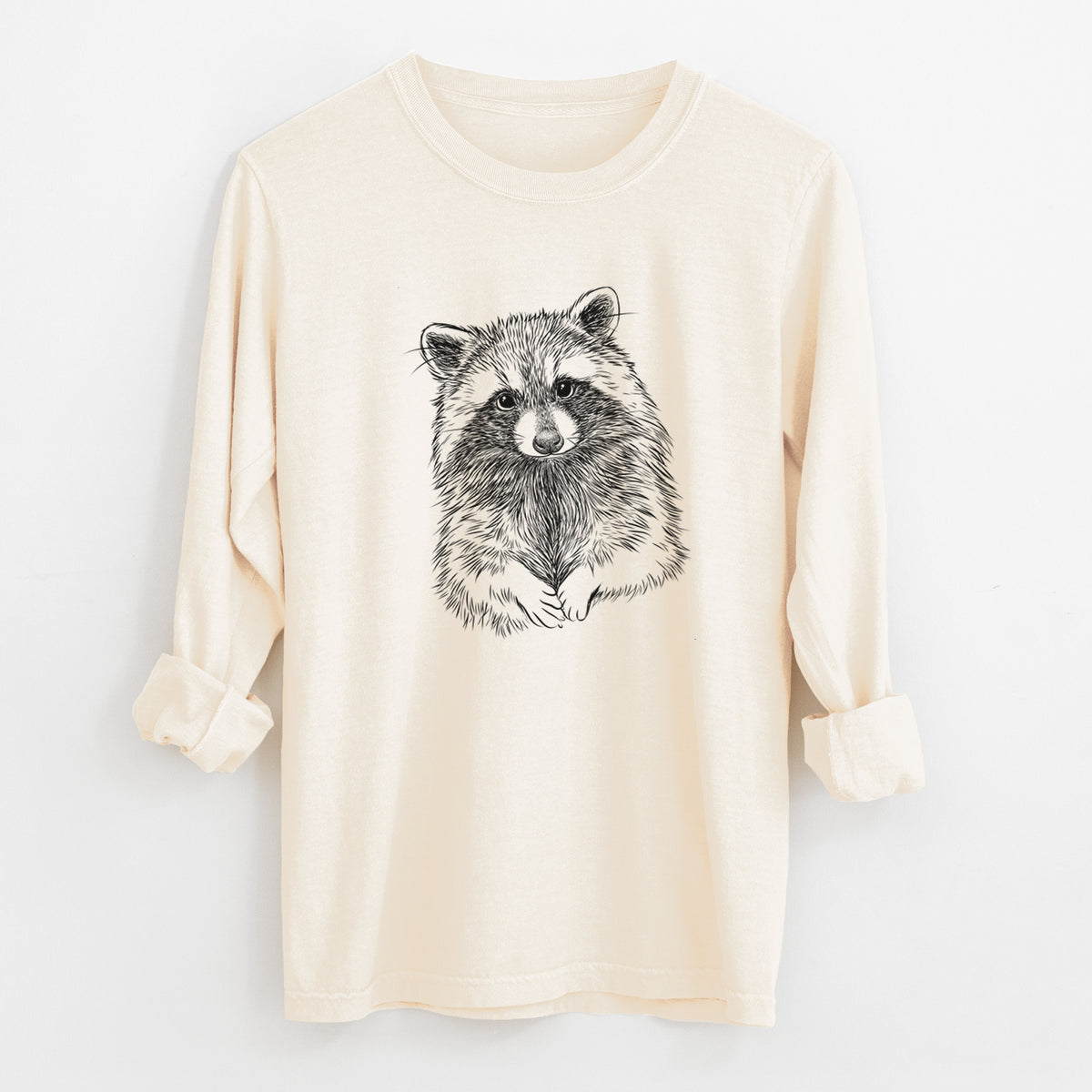 Ivory Comfort Colors long sleeve shirt laid flat with the cuffs rolled, printed with a detailed black ink portrait of a raccoon with its front paws resting in front of it.