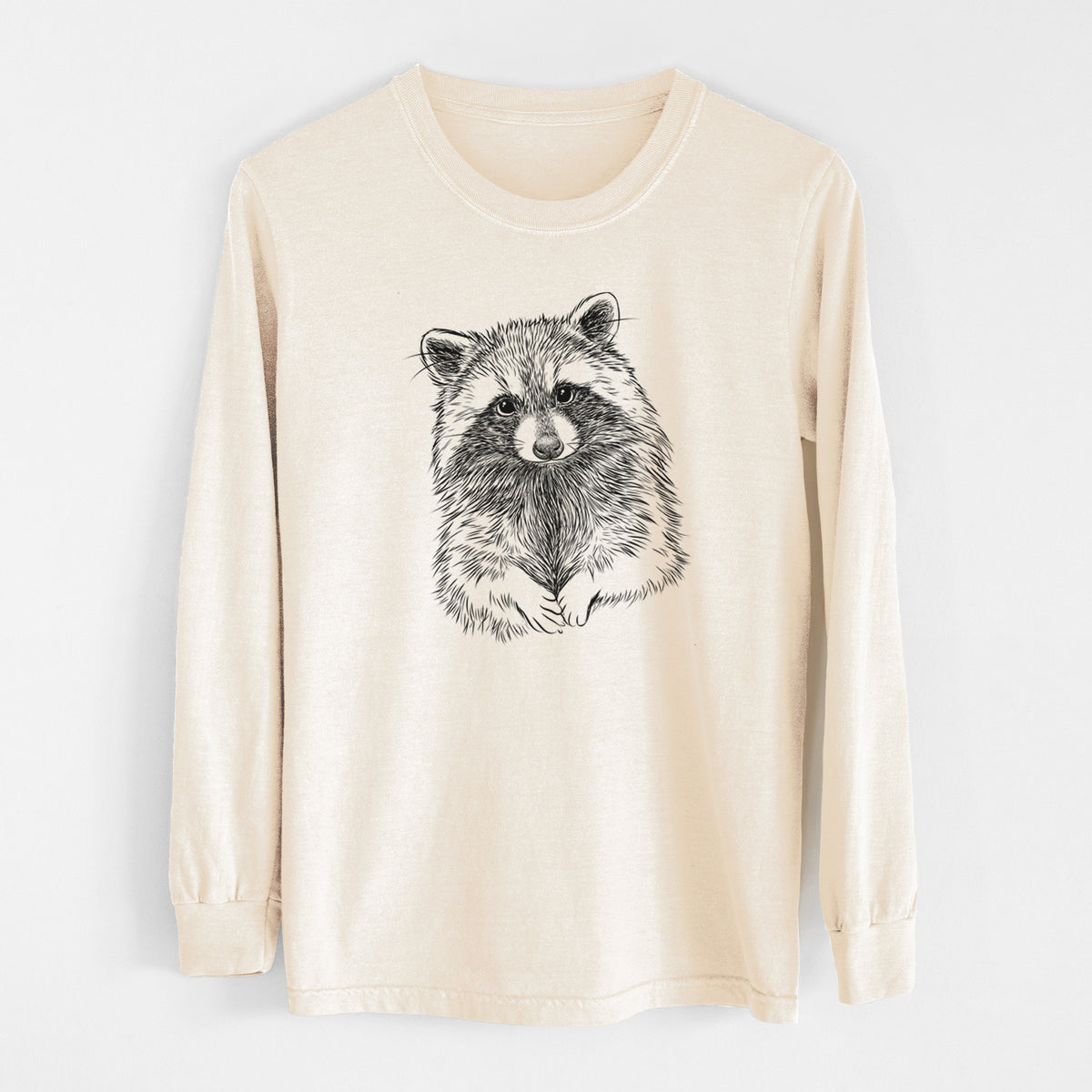 Ivory Comfort Colors long sleeve shirt laid flat, printed with a detailed black ink portrait of a raccoon with its front paws resting in front of it.