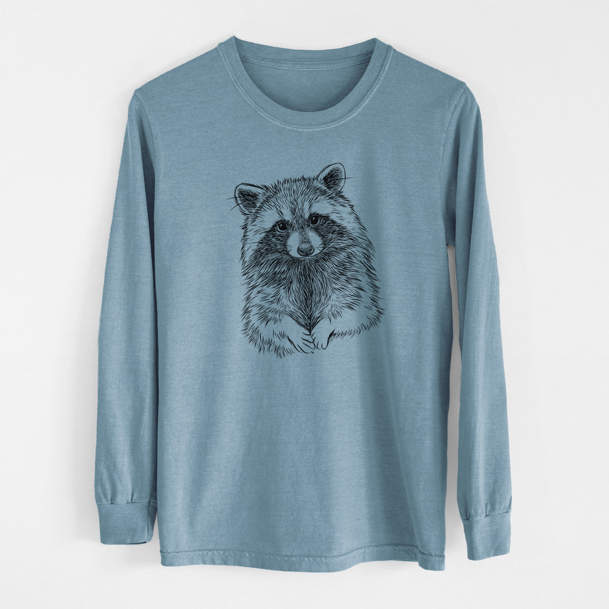 Steel blue Comfort Colors long sleeve shirt laid flat, printed with a detailed black ink portrait of a raccoon with its front paws resting in front of it.