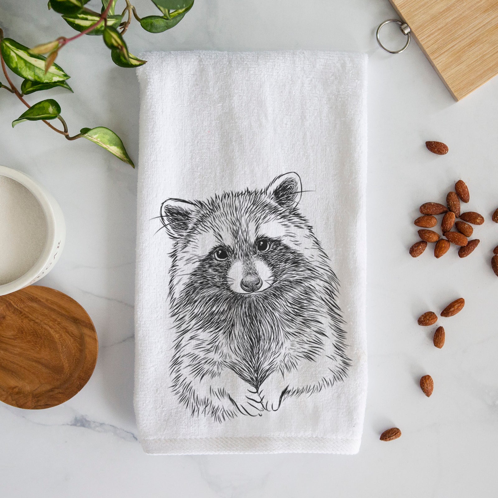 White hand towel printed with a detailed black ink portrait of a raccoon with its front paws resting in front of it.