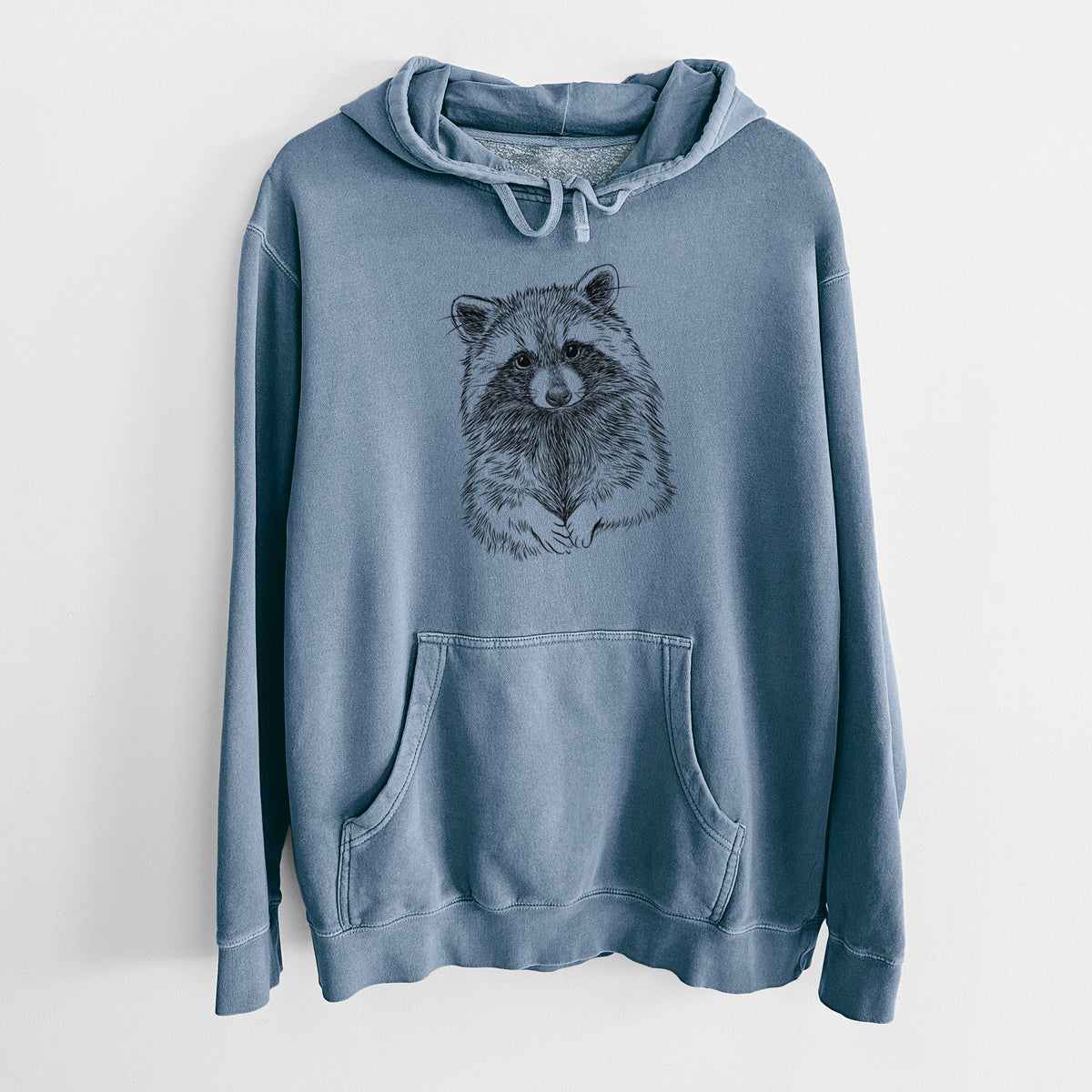Slate blue pigment dyed hoodie laid flat, printed with a detailed black ink portrait of a raccoon with its front paws resting in front of it.