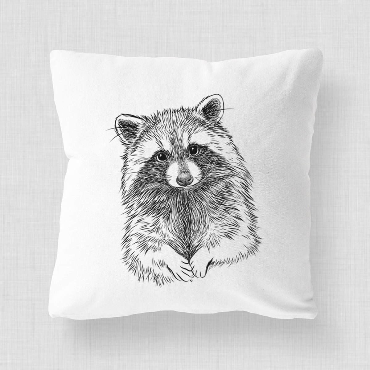 White pillow cover printed with a detailed black ink portrait of a raccoon with its front paws resting in front of it.