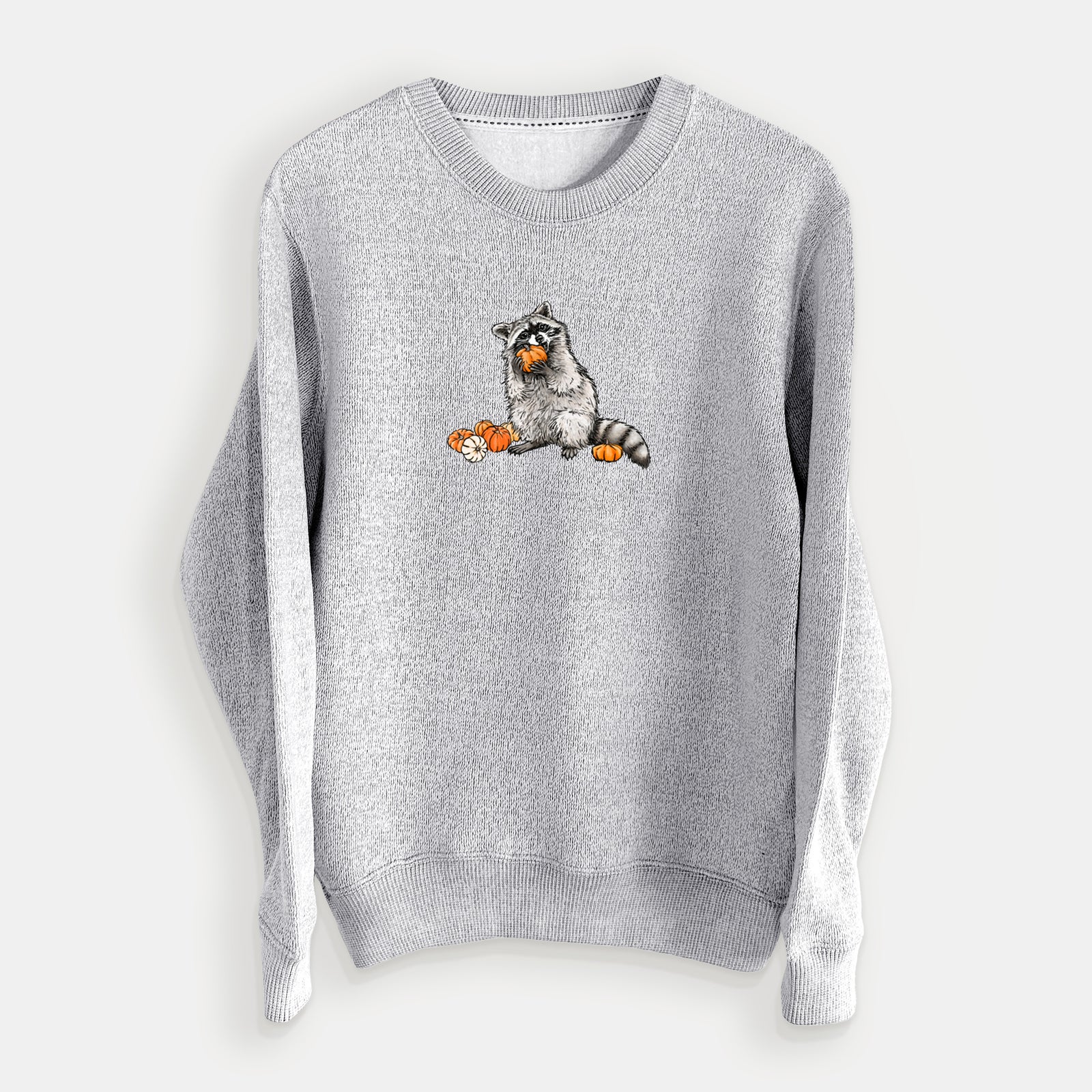 Salt and pepper knit sweatshirt laid flat, printed with a black ink raccoon eating a small orange pumpkin, with more pumpkins beside it.