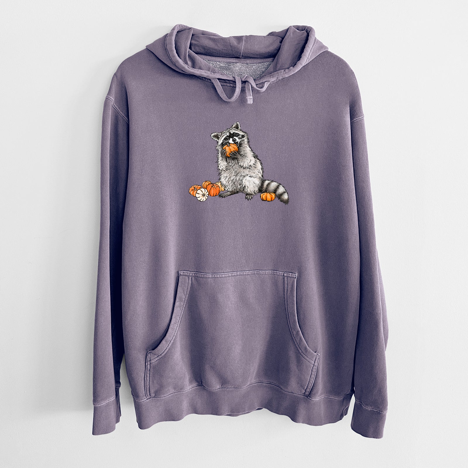 Plum purple pigment dyed hoodie laid flat, printed with a black ink raccoon eating a small orange pumpkin, with more pumpkins beside it.