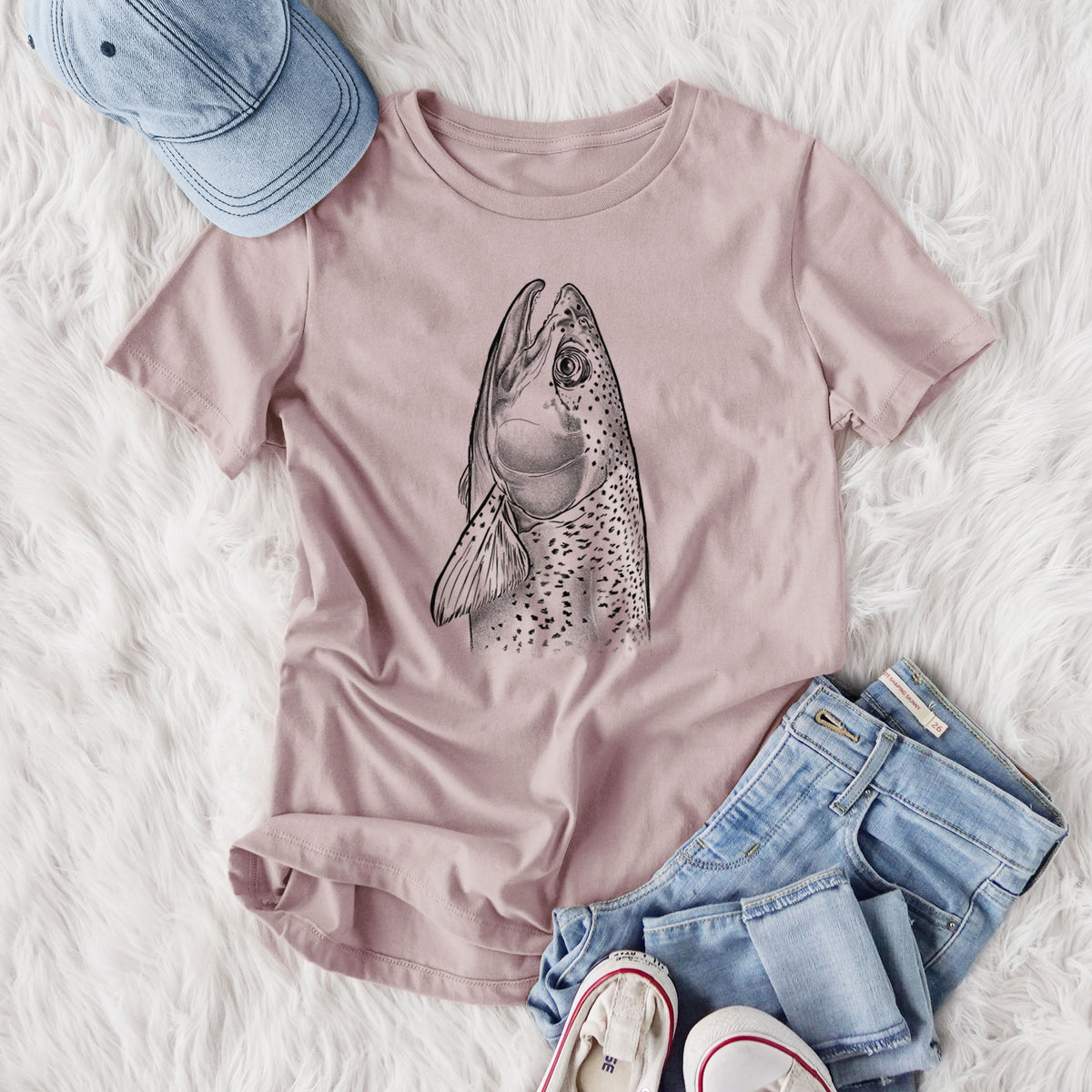 Women's relaxed fit cotton t-shirt printed with a detailed black ink illustration of a rainbow trout's head pointing upward, showing its spotted scales, styled flat on a white faux fur rug with jeans.