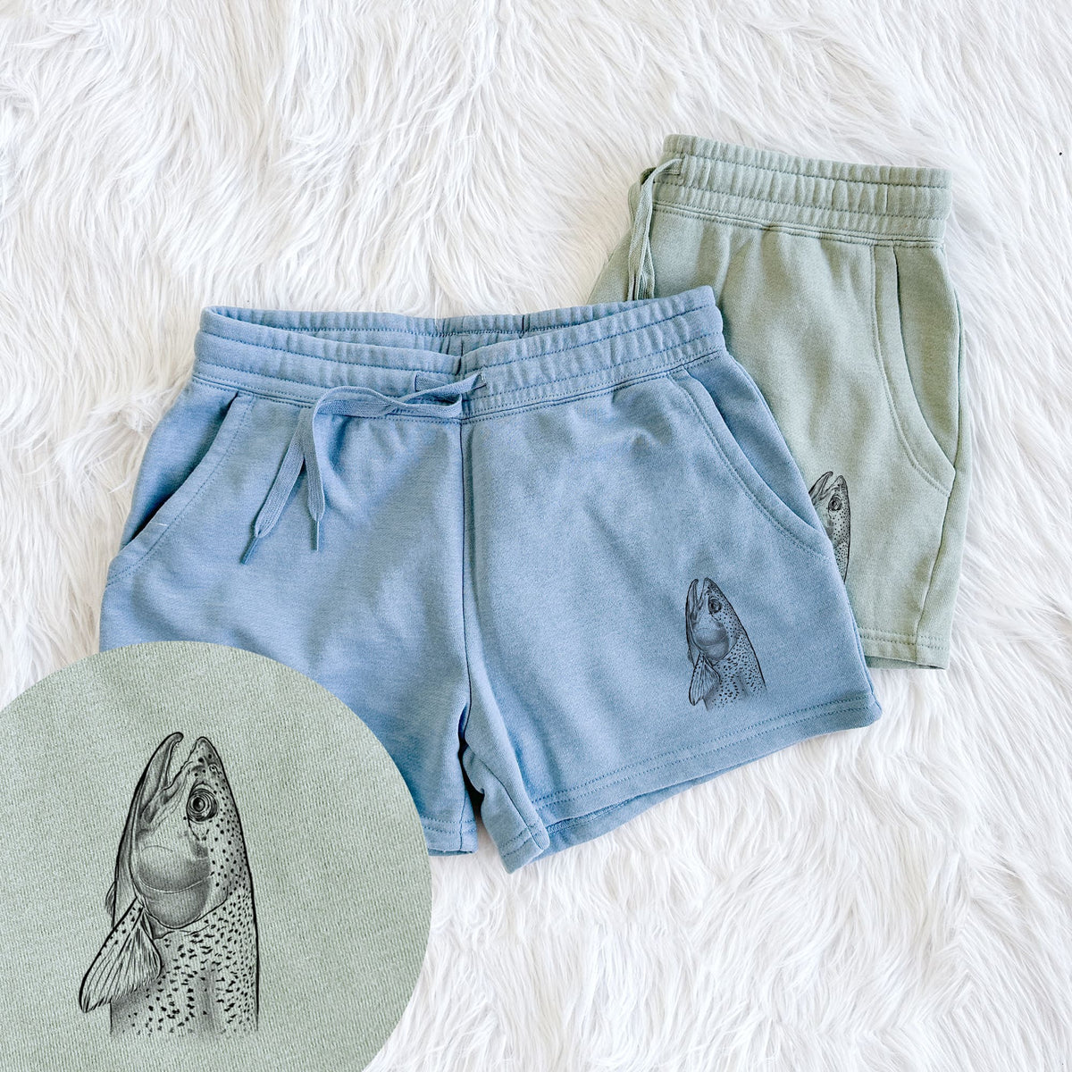 Two pairs of Cali Wave shorts in different colors printed with a detailed black ink illustration of a rainbow trout's head pointing upward, showing its spotted scales, with a close-up of the print.