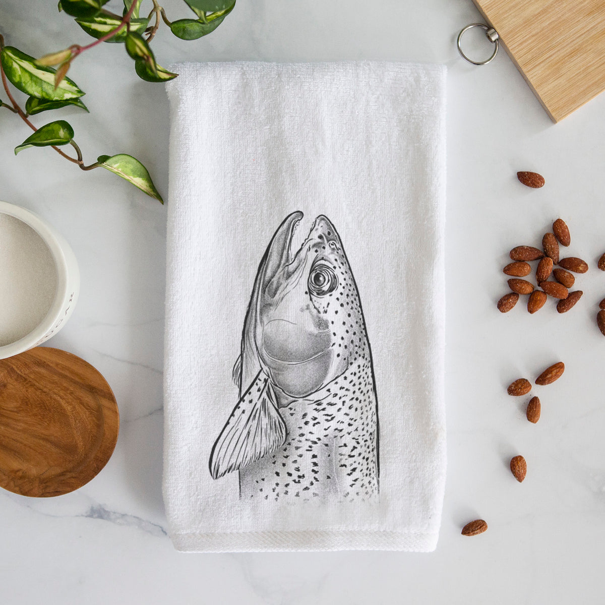 White hand towel printed with a detailed black ink illustration of a rainbow trout's head pointing upward, showing its spotted scales.