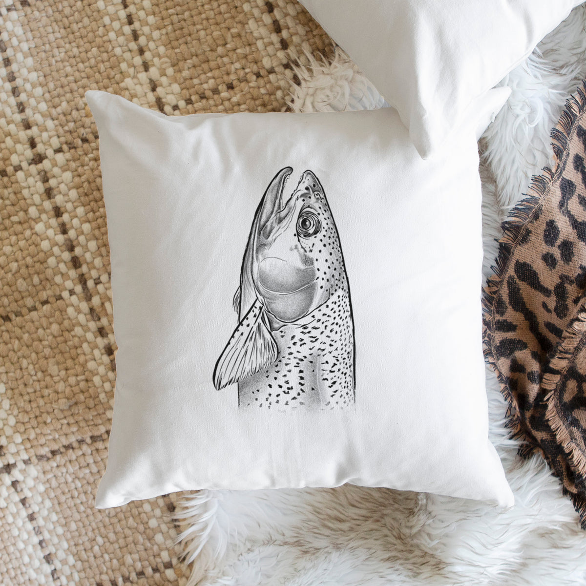White pillow cover printed with a detailed black ink illustration of a rainbow trout's head pointing upward, showing its spotted scales, on a woven chair.
